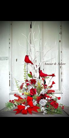 a vase filled with red flowers and birds sitting on top of a wooden table next to a white door