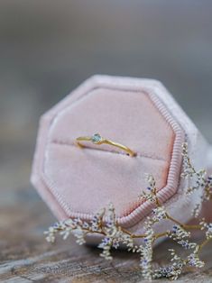 a pink velvet box with a ring on it and some white flowers in the corner