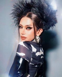 a woman with black feathers on her head posing for a magazine cover photo in front of a gray background