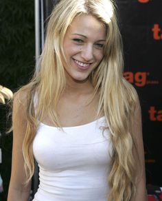 a woman with long blonde hair standing in front of a sign and smiling at the camera