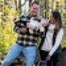 a man and woman standing next to each other in front of a forest with trees