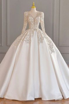 a white wedding dress with long sleeves and lace on the skirt is displayed in front of a