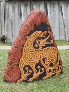 a decorative rock in the shape of a horse on grass with a wooden fence behind it