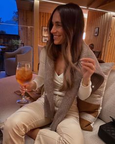 a woman sitting on a couch with a glass of wine in her hand and smiling