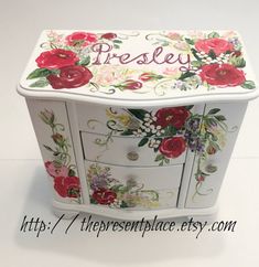 a white dresser with red flowers painted on the drawers and name presly written on it