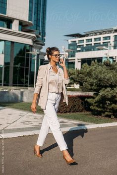 a woman is walking down the street talking on her cell phone while wearing white pants