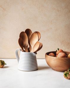 wooden spoons and bowls with strawberries in them on a white countertop next to a beige wall