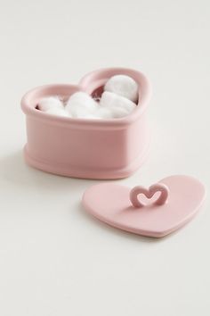 two pink containers with cotton in them on a white surface, one has a heart shaped container