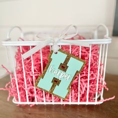 a basket filled with pink shredded grass and a wooden letter hanging from the front of it