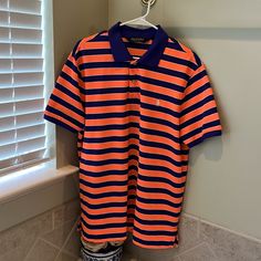 an orange and blue striped polo shirt hanging on a rack in front of a window