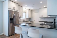 a modern kitchen with stainless steel appliances and white cabinetry, along with bar stools