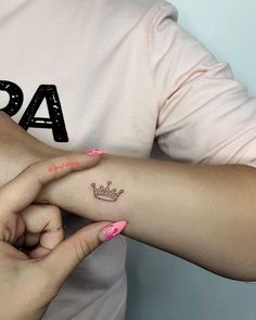 two hands holding each other with small tattoos on their arms and wrist, one has a crown tattoo on it's left arm