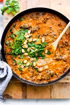 a skillet filled with stew and garnished with cilantro, parsley and pine nuts