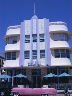 an old pink car parked in front of a tall building with blue and white trim