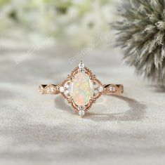 an opal and diamond ring sits on a table next to a pine tree branch