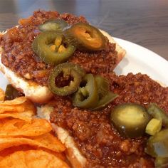 a chili cheeseburger with pickles and chips on a white plate, ready to be eaten