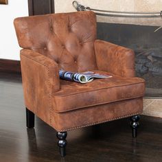 a brown chair sitting in front of a fire place with a magazine on it's arm