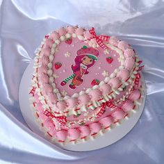 a pink cake with white frosting and red decorations on the top is sitting on a plate