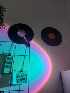 two vinyl records are hanging on the wall in front of a mirror with rainbow lights