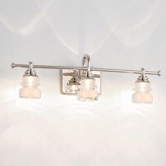 three light bathroom fixture with clear glass shades on the sides and chrome finish, against a white background