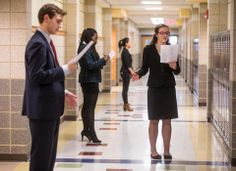 three people in business attire are talking to each other on the hallway between two buildings