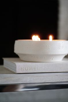 two lit candles sitting on top of a book with the word home written across it