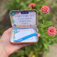 a person holding a small tin with a pen in it and some flowers behind it