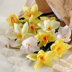 some yellow and white flowers are sitting on a table cloth next to a brown paper bag