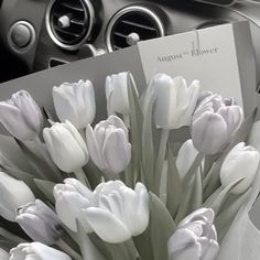 a bouquet of white tulips sitting on top of a table next to a car dashboard