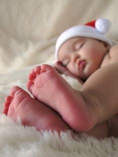 a baby wearing a santa hat laying on top of a white blanket