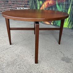 a wooden table sitting on top of a sidewalk next to a wall with a painting