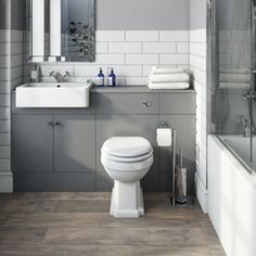 a white toilet sitting next to a bath tub under a bathroom mirror on top of a wooden floor