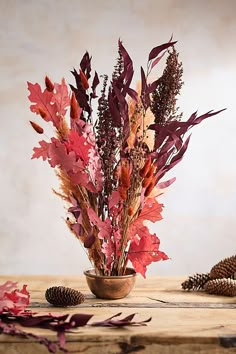 a vase filled with lots of different types of leaves and flowers on top of a wooden table