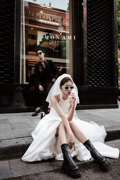 a woman sitting on the ground in front of a store wearing sunglasses and a wedding dress