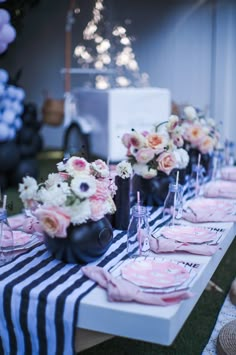 the table is set with pink and white flowers in black vases, striped napkins, and silverware