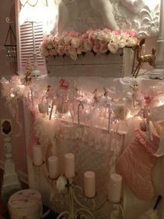 a white mantle with candles and pink flowers on it in front of a mirror that is decorated with angel wings