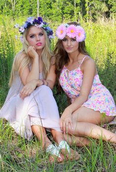 two beautiful young women sitting next to each other in the grass with flowers on their heads