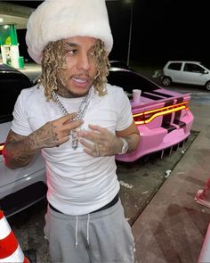 a man with long hair wearing a white hat and standing next to a pink car