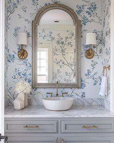 a bathroom with blue and white wallpaper, gold faucet, marble counter top