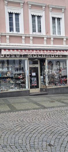 a store front with many items on display in it's windows and the sidewalk is made of cobblestone