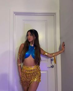 a woman in a gold and blue costume standing next to a door with her hands on her hips