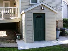 a small house with a green door next to a white fence and steps leading up to it