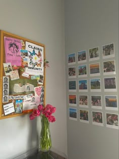 a vase filled with pink flowers sitting on top of a table next to a bulletin board