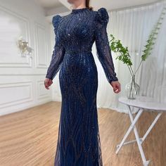 a woman in a long blue dress standing on a wooden floor next to a table