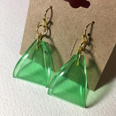 a pair of green earrings sitting on top of a piece of brown paper next to a card