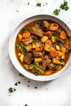 a white bowl filled with stew and carrots on top of a marble countertop