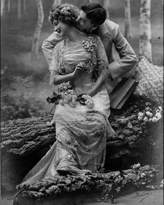 an old fashion photo of two women sitting on a tree trunk in the woods, kissing