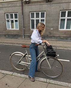 a woman standing next to a bike with a basket on the front and back wheels