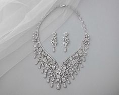 This elegant set features a statement-style floral design, perfect for weddings. Crafted with rhodium-plated copper and adorned with high quality AAA CZ stones, it adds a touch of glamour to any ensemble.

lead, nickel, and cadmium free
AAA CZ stones
rhodium plated
necklace length is 15.5 inches, 2 inch extender included
earrings are post pierced and are 1.75 inches long Gold Headpiece, Headpiece Hairstyles, Vintage Inspired Jewelry, Plate Necklace, Elegant Sets, Cz Necklace, Wedding Jewelry Sets, Cz Stone, Necklace Length