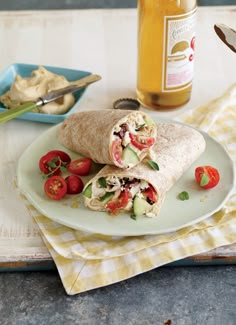 two wraps on a plate with tomatoes, cucumber and mustard in the background